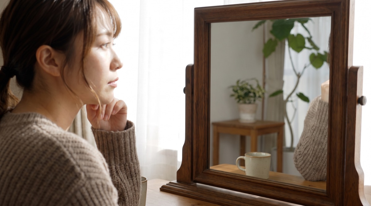 鏡を見ながら、脂肪吸引と脂肪溶解注射のどちらを選ぶか、あるいは試してから決めるか考えている女性